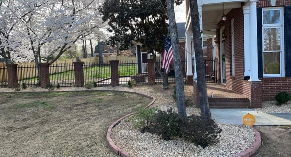 Charming brick home with American flag, blooming trees, and landscaped garden.