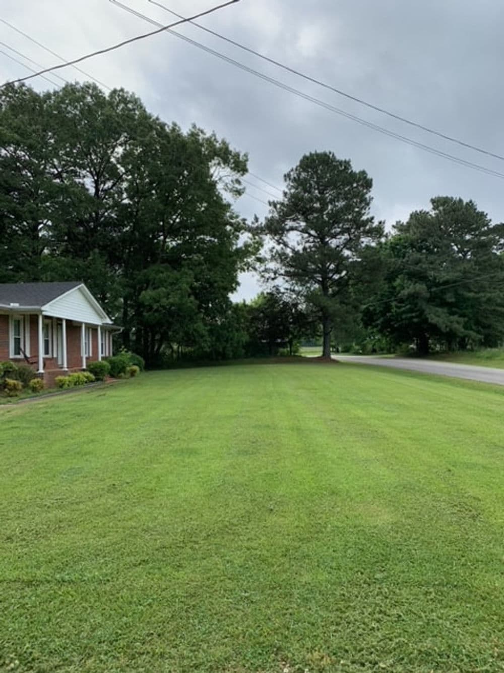Lawn with well-maintained grass and trees beside a house under a cloudy sky.