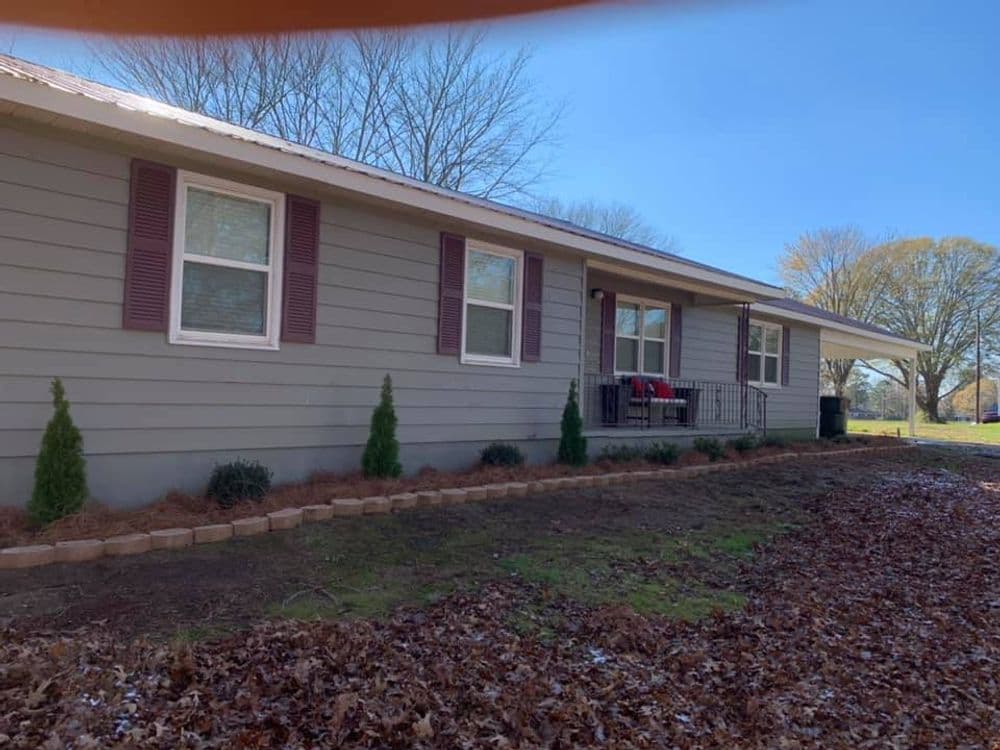 Single-story gray house with front porch, landscaped yard, and fall leaves in the foreground.