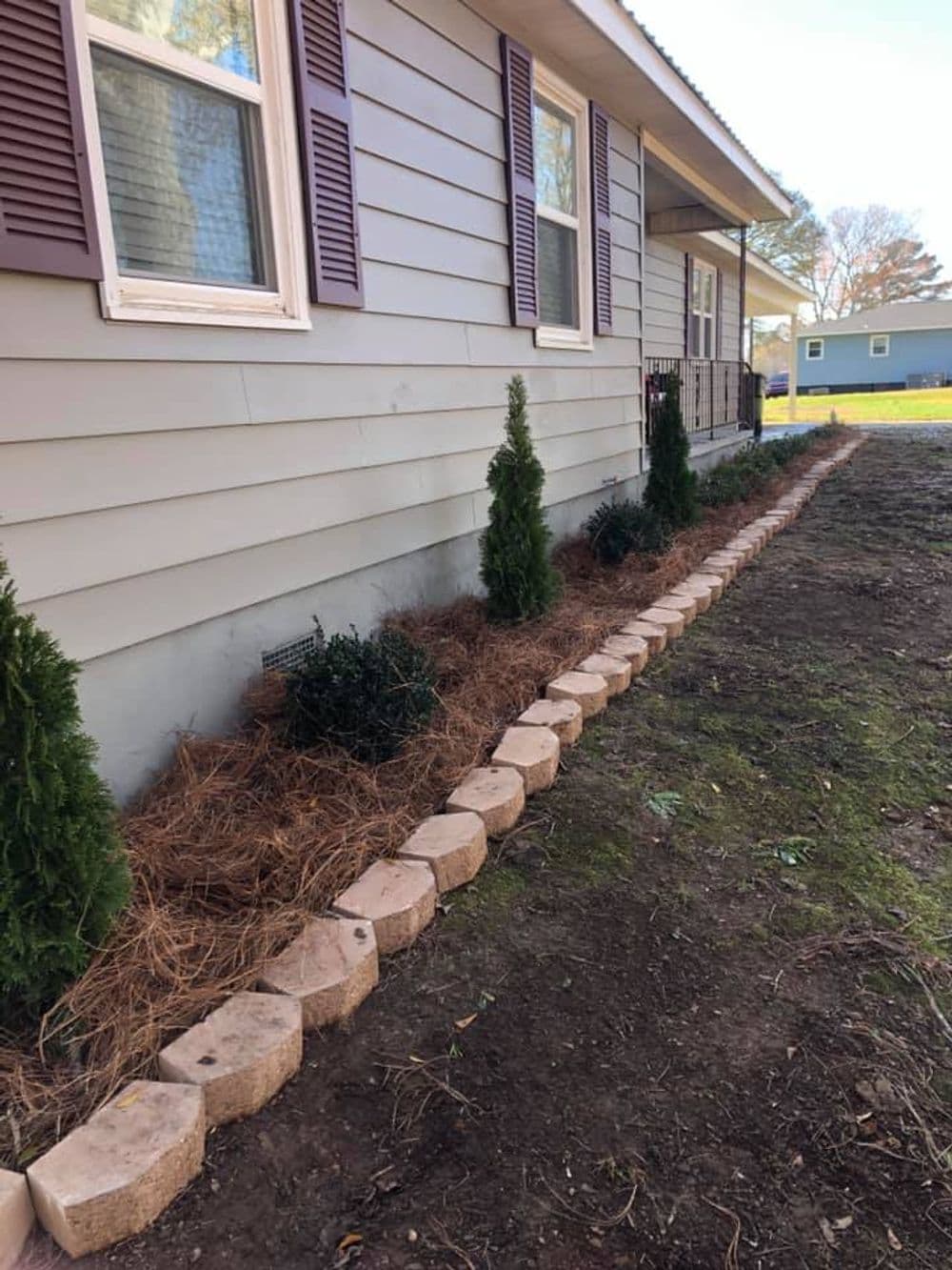 Lush landscaping with shrubs and stone border along a house exterior.
