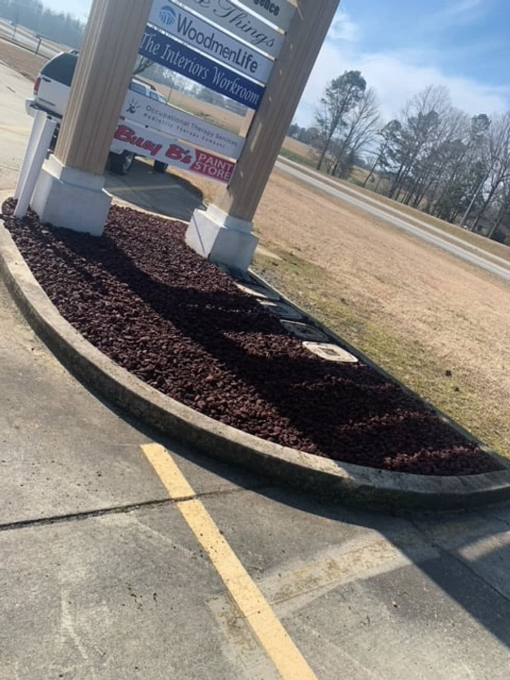Sign for WoodmenLife and Buy By Paint Store with landscaping and gravel parking area.