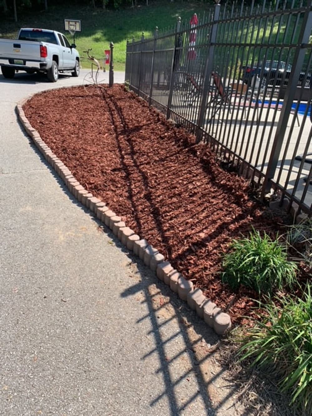 Mulched garden bed with stone edging beside a paved path and a fence in a residential area.