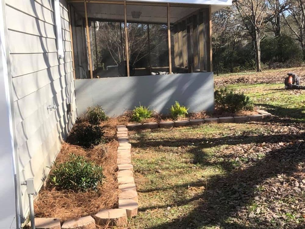 Landscaped garden bed with stone border and shrubs beside a screened porch.
