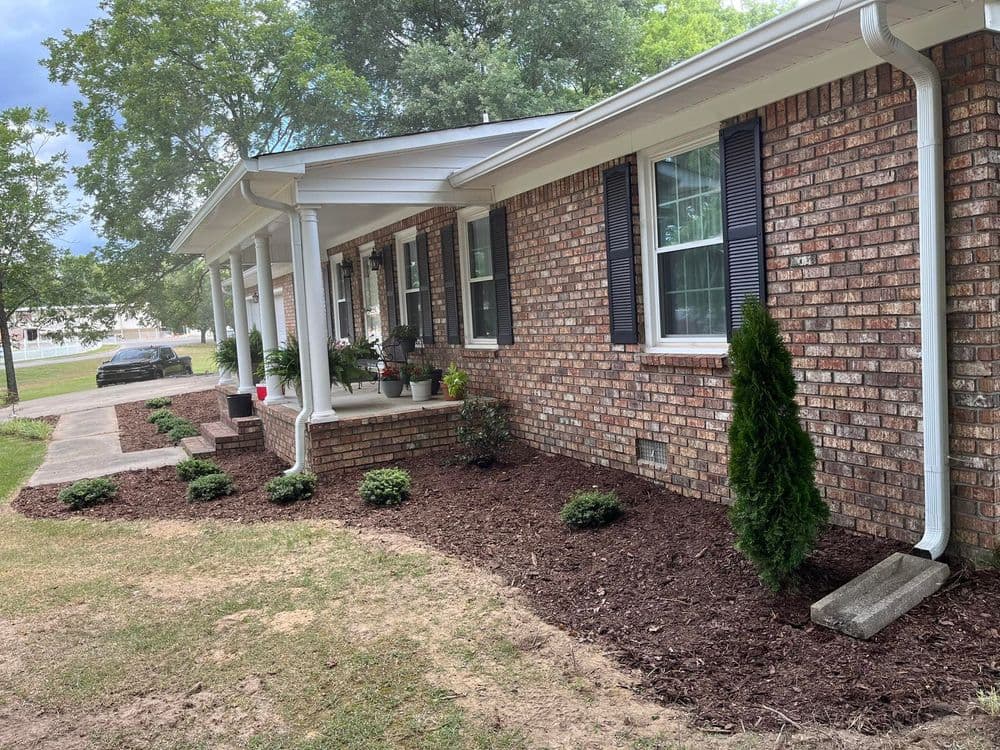 Charming brick home with landscaped front yard and porch, featuring shrubs and flower pots.