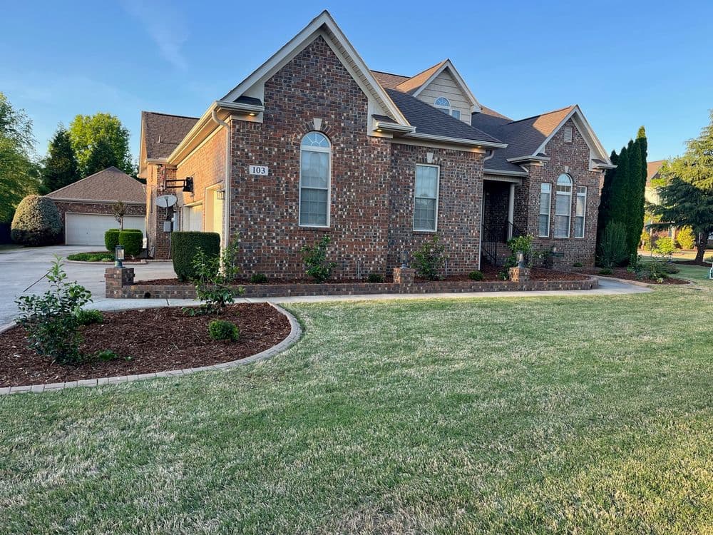 Brick house with landscaped front yard and neatly trimmed lawn in a residential area.
