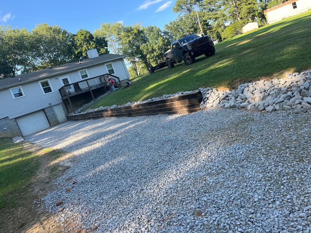 Gravel driveway and landscaping near a house with a parked black truck and green lawn.