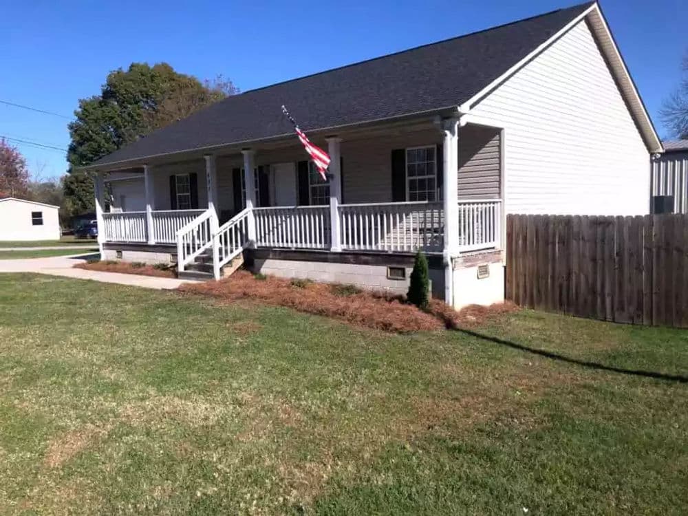 Front view of a charming house with a porch, American flag, and landscaped yard.