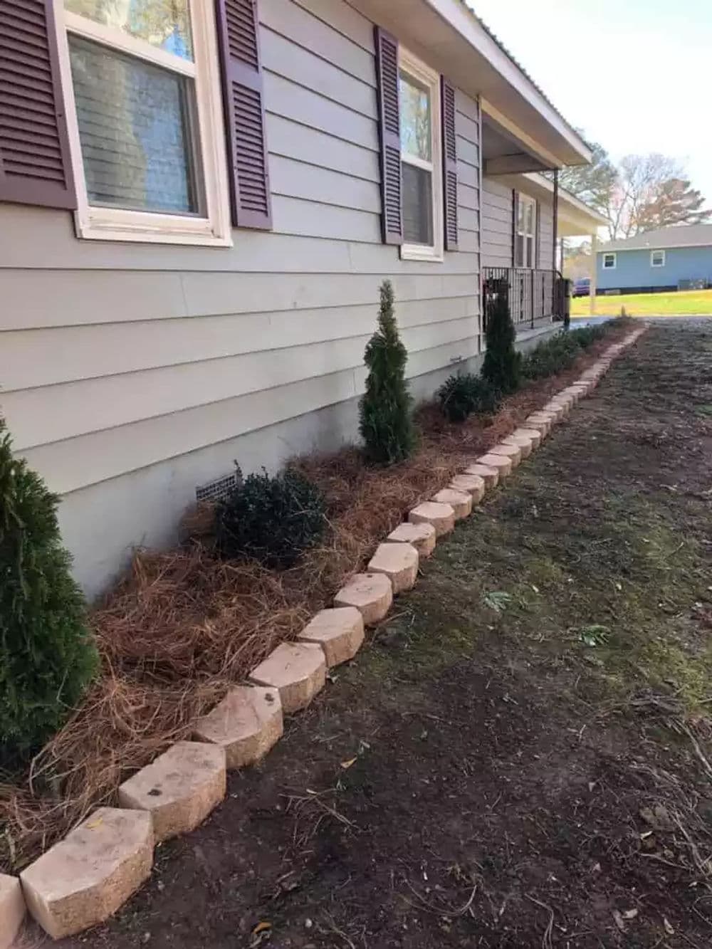 Landscaped home exterior with stone edging, evergreen plants, and fresh pine straw mulch.