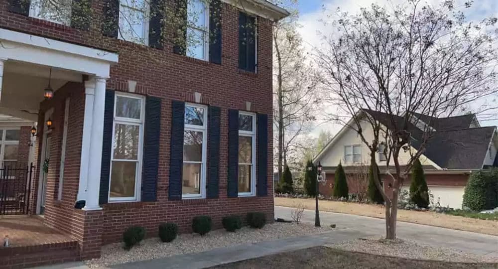 Brick home with black shutters and landscaped yard, showcasing nearby driveway and trees.
