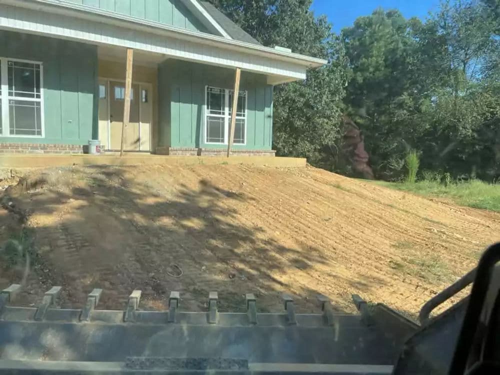 Newly graded land for house construction with green siding and clear blue sky.