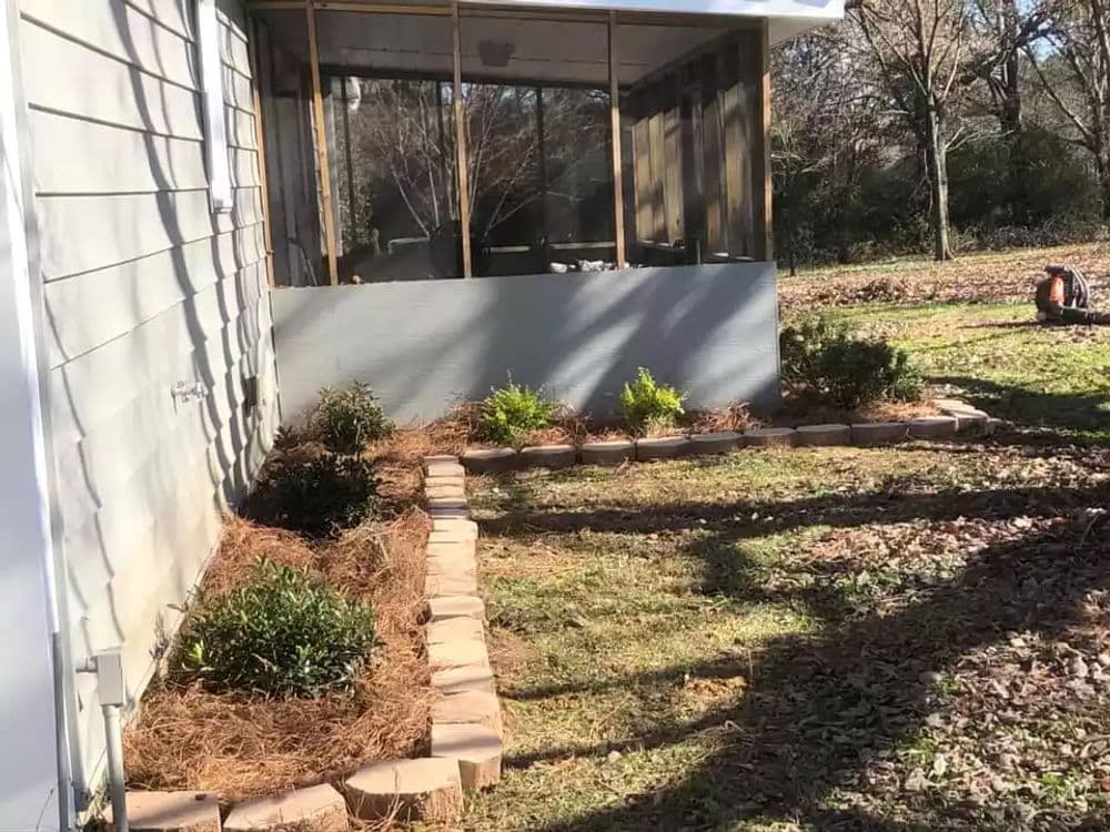 Landscaped garden with stone border, green plants, and a screened porch in the background.