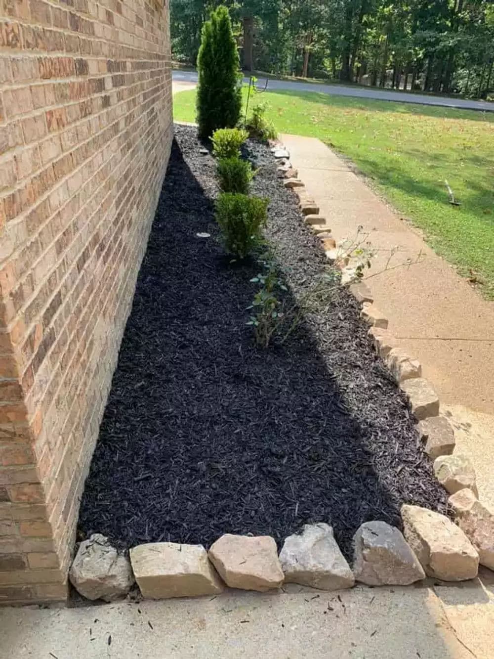 Landscape design featuring mulched garden bed with shrubs and stone edging along a brick wall.