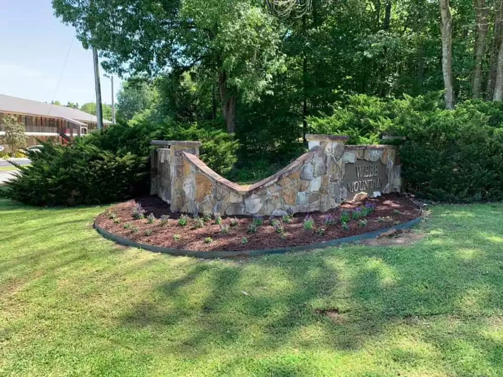 Stone monument sign for Wilderness Mountain, surrounded by greenery and flowers.