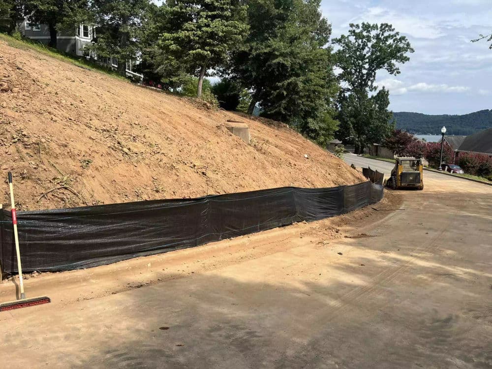 Construction site with a bulldozer and erosion control barrier on a hillside road.