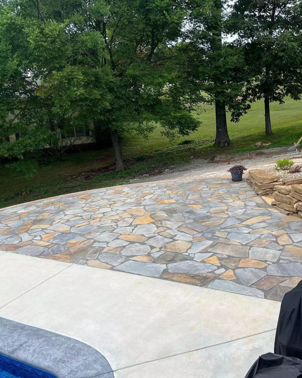Stunning outdoor stone patio surrounded by lush green trees and grass. Ideal for gatherings.
