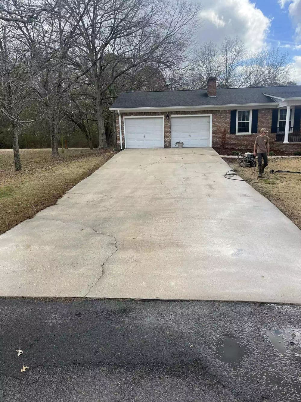 Driveway with cracks, leading to a house with two garages, surrounded by bare trees.