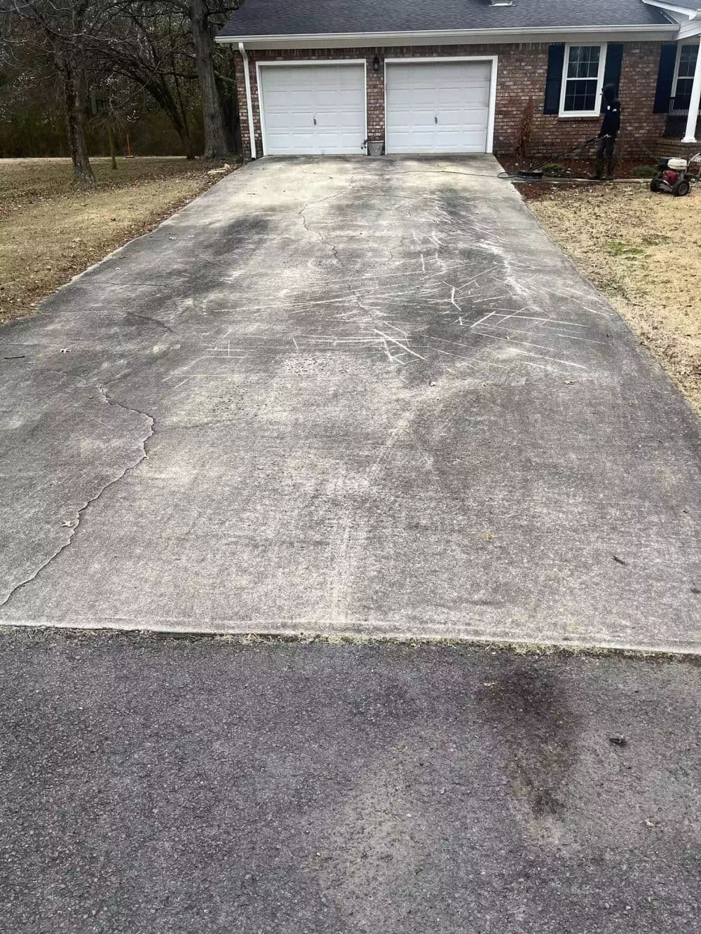 Concrete driveway leading to a brick garage, showing visible cracks and wear.