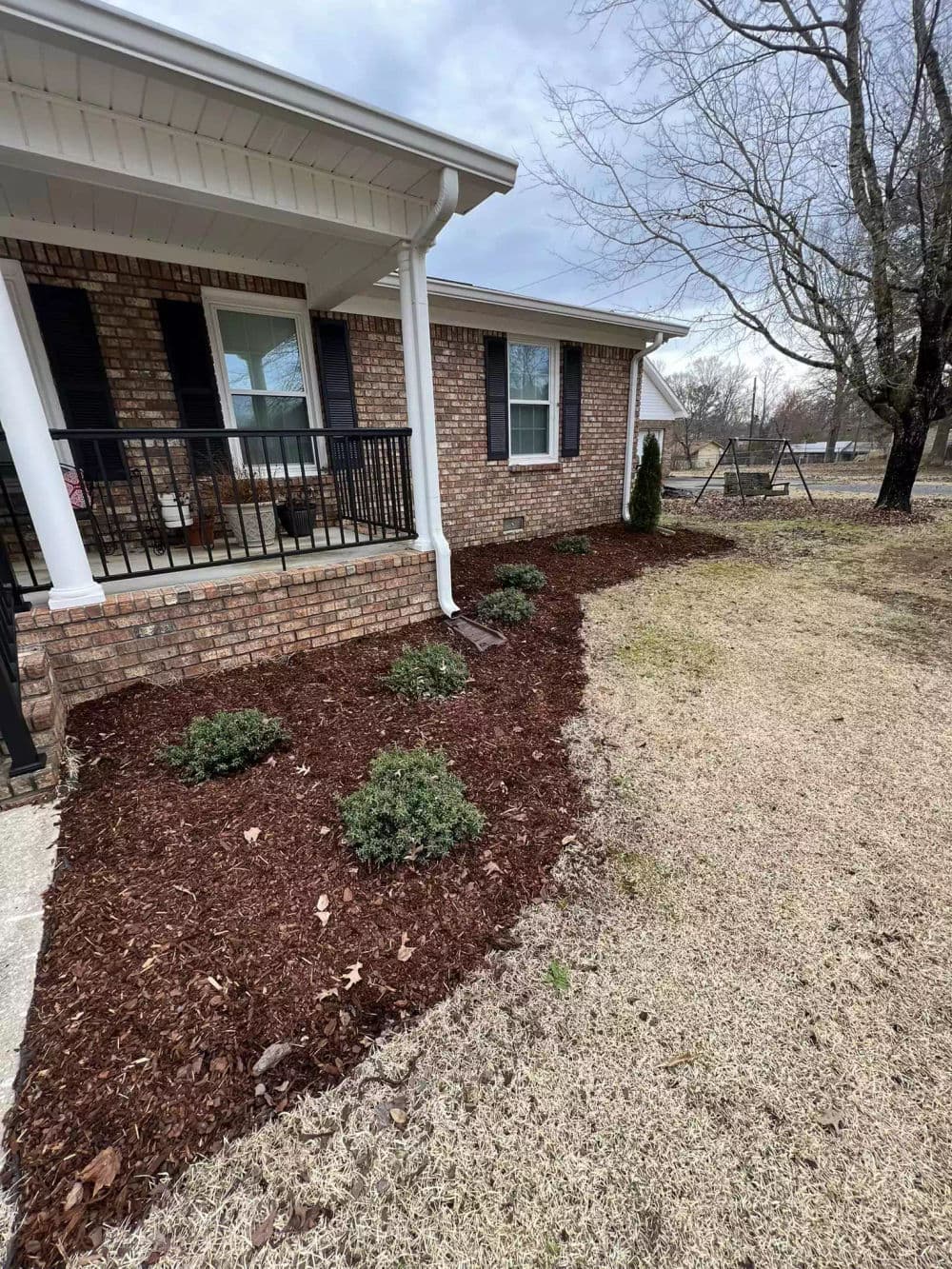Brick house exterior with landscaped garden, fresh mulch, and green shrubs on cloudy day.