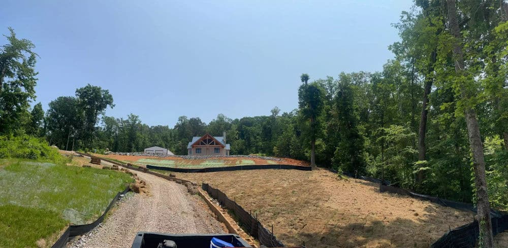 New home construction site in a wooded area with cleared land and erosion control measures.