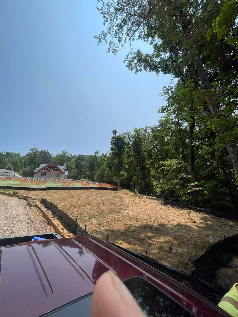 Newly cleared hillside with a house in background, surrounded by trees and construction materials.