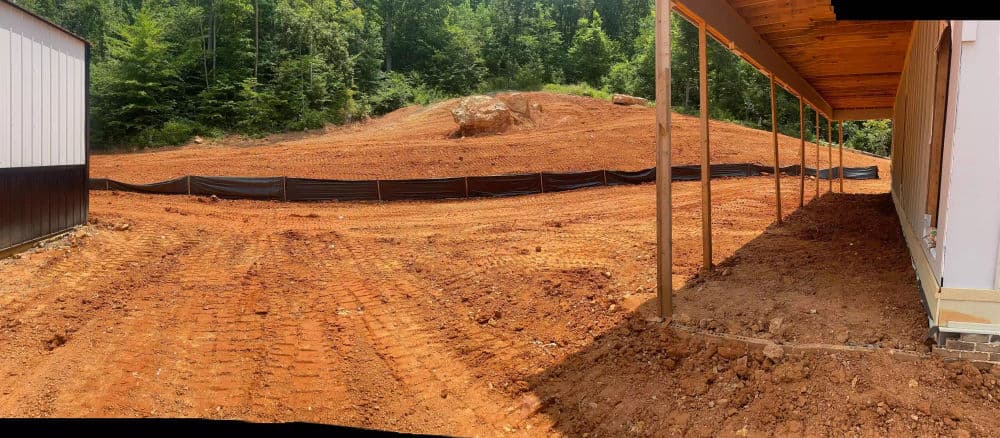 Cleared construction site with bare soil, surrounding greenery, and protective fencing.